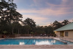 Una piscina con sillas de descanso y sombrillas, rodeada de árboles y una valla de madera.