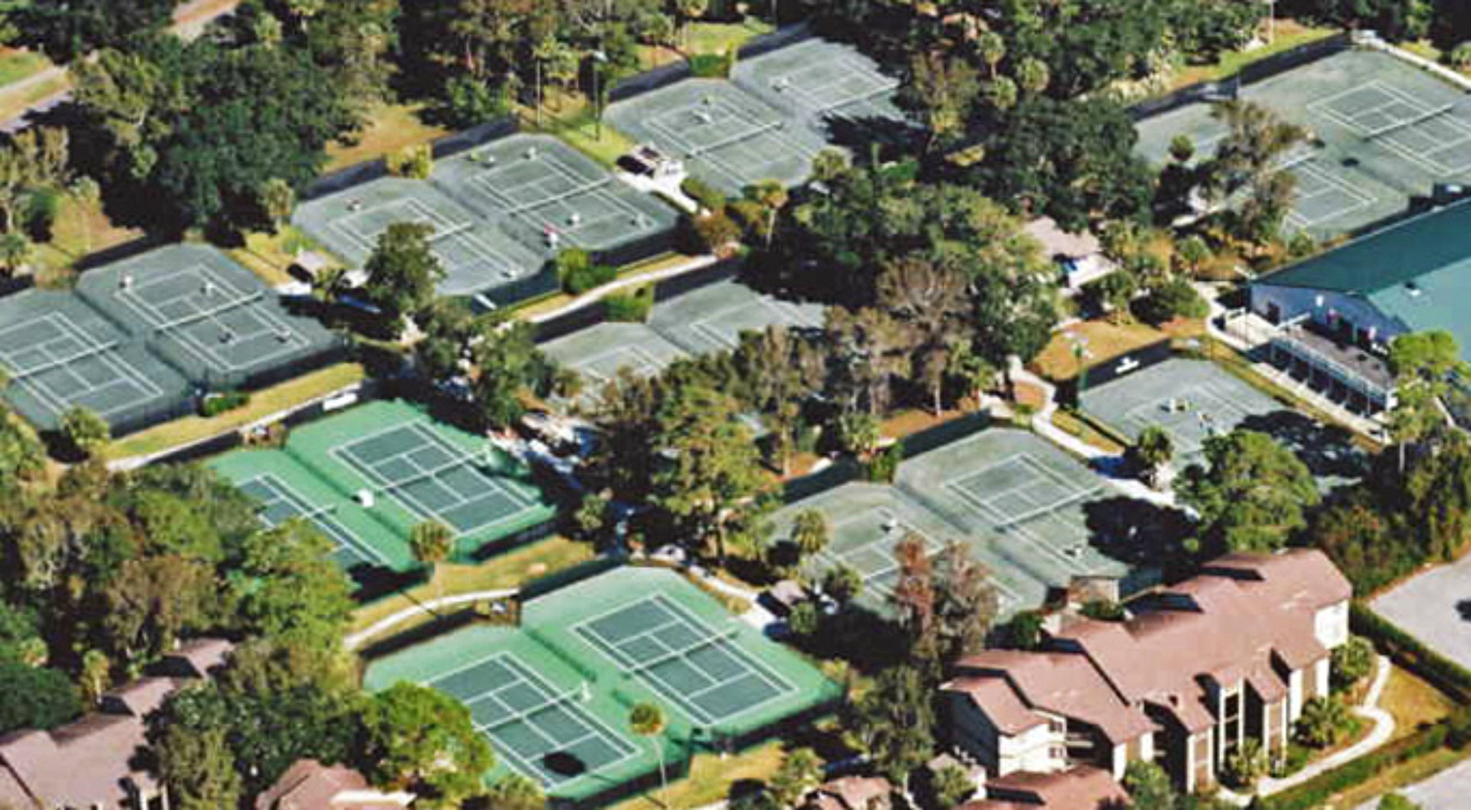 An aerial view of a residential area with multiple tennis courts surrounded by houses and greenery.