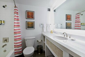 Un baño moderno con lavamanos, inodoro y cortina de ducha blancos. Hay cuadros en la pared y un cubo de basura.
