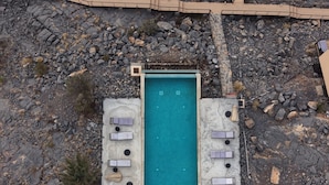 An aerial view of a resort with a central swimming pool, multiple lounge areas with sun loungers, and two small buildings with flat roofs. - The View (Al Hamra)