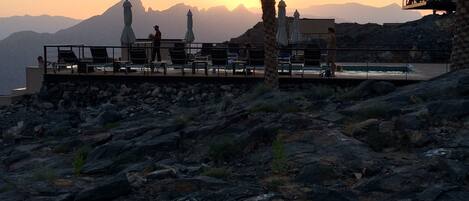 Terraza con mobiliario exterior y vistas a montañas al atardecer.