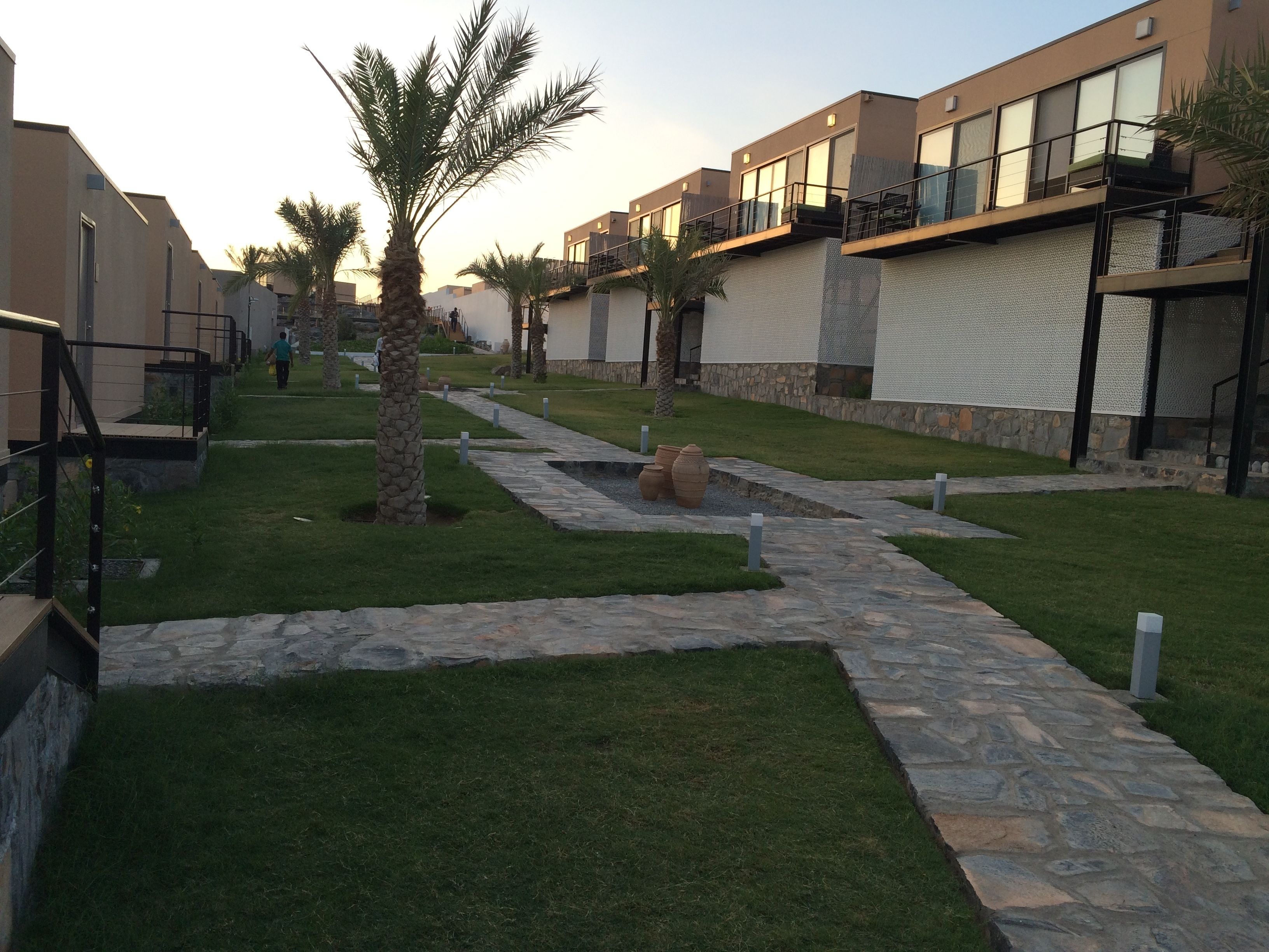 A modern residential complex with stone pathways, palm trees, and a clear sky.