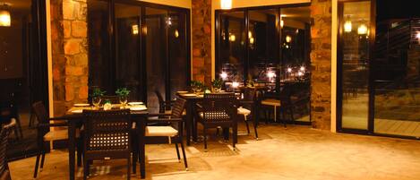 Un comedor con pared de piedra, ventanas amplias y lámparas colgantes.