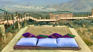A high vantage point with a view of a valley and mountains. There is a set of stairs leading to a building with a balcony. - The View (Al Hamra)