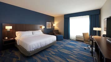 Una habitación de hotel con una cama grande, un escritorio, una silla, una lámpara de escritorio, un televisor montado en la pared y una ventana con cortinas.