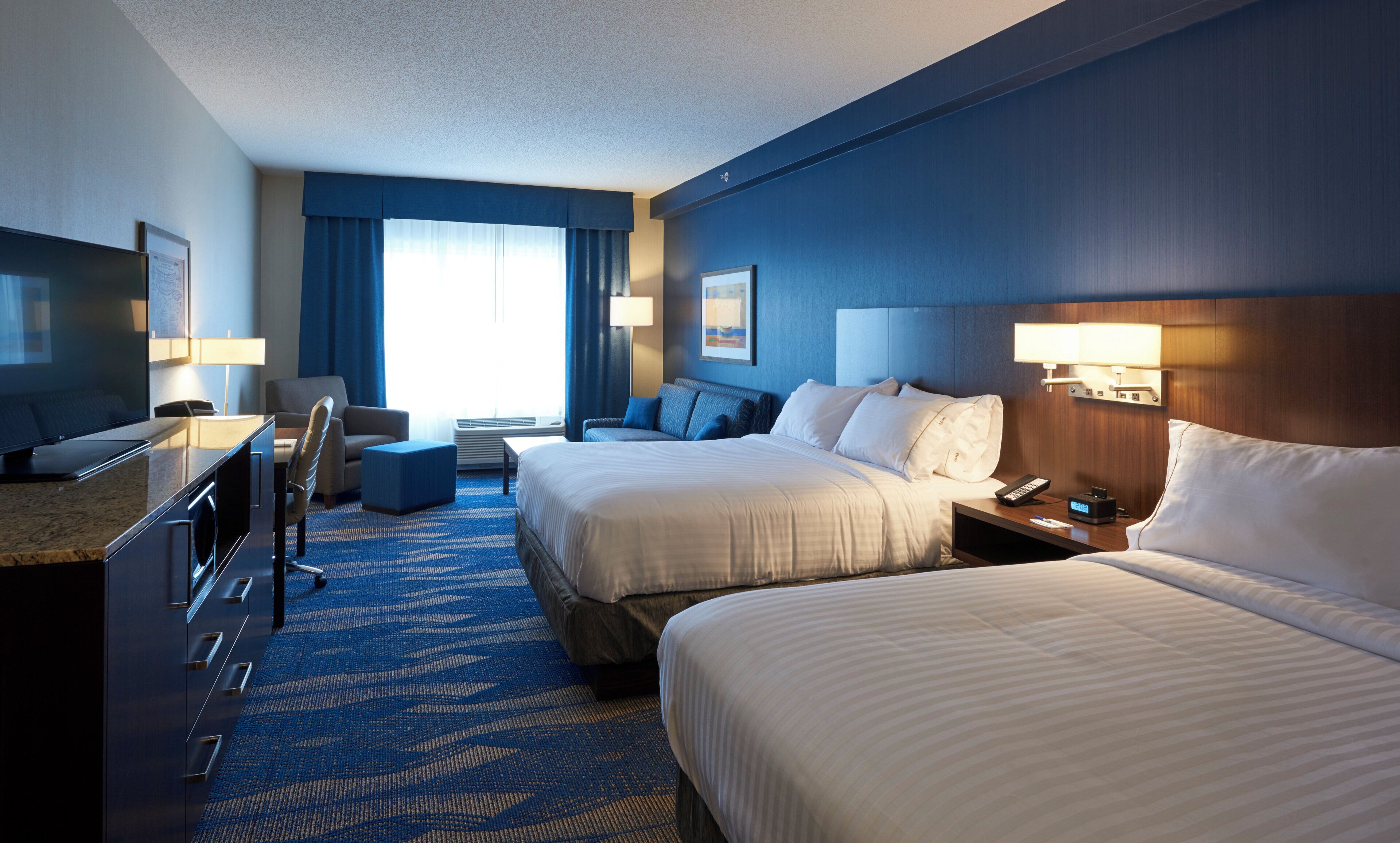 A hotel room with two beds, a desk, a chair, a TV, and a window with curtains.