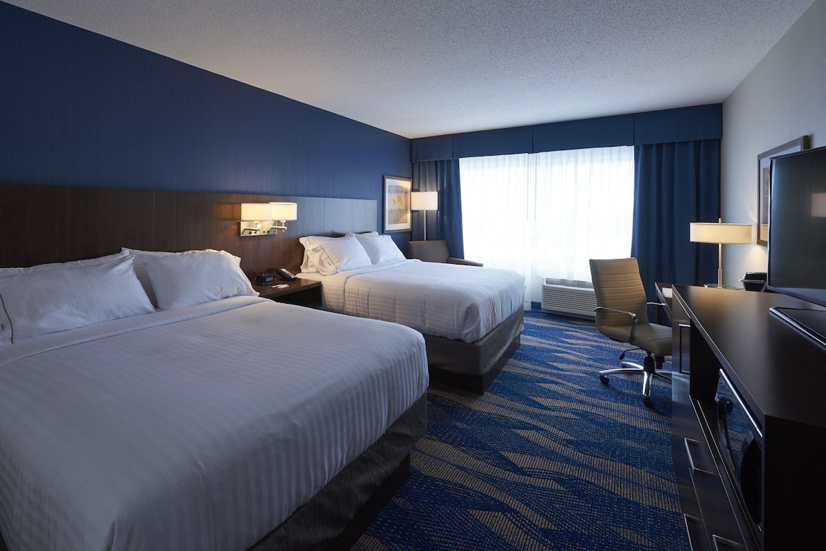 A hotel room with two beds, a desk, a chair, a TV, and a window with curtains.