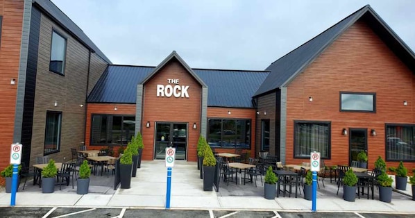 A building with a sign reading "The Rock" and outdoor seating with potted plants.