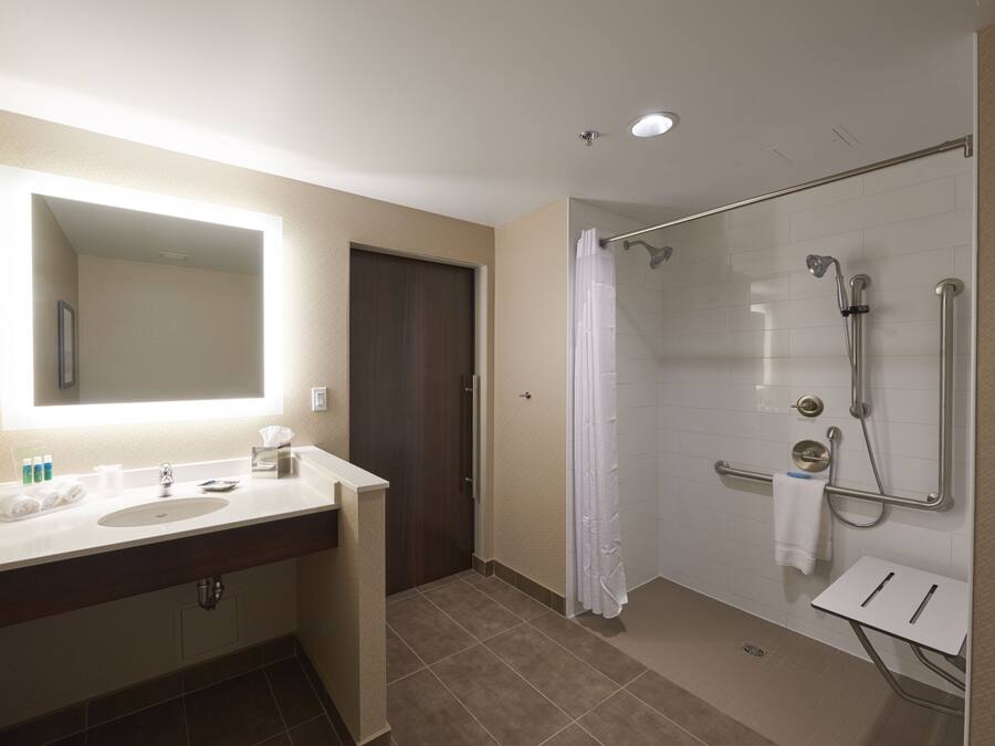 A modern bathroom with a large mirror, two sinks, a shower with a glass door, and a small vanity table.