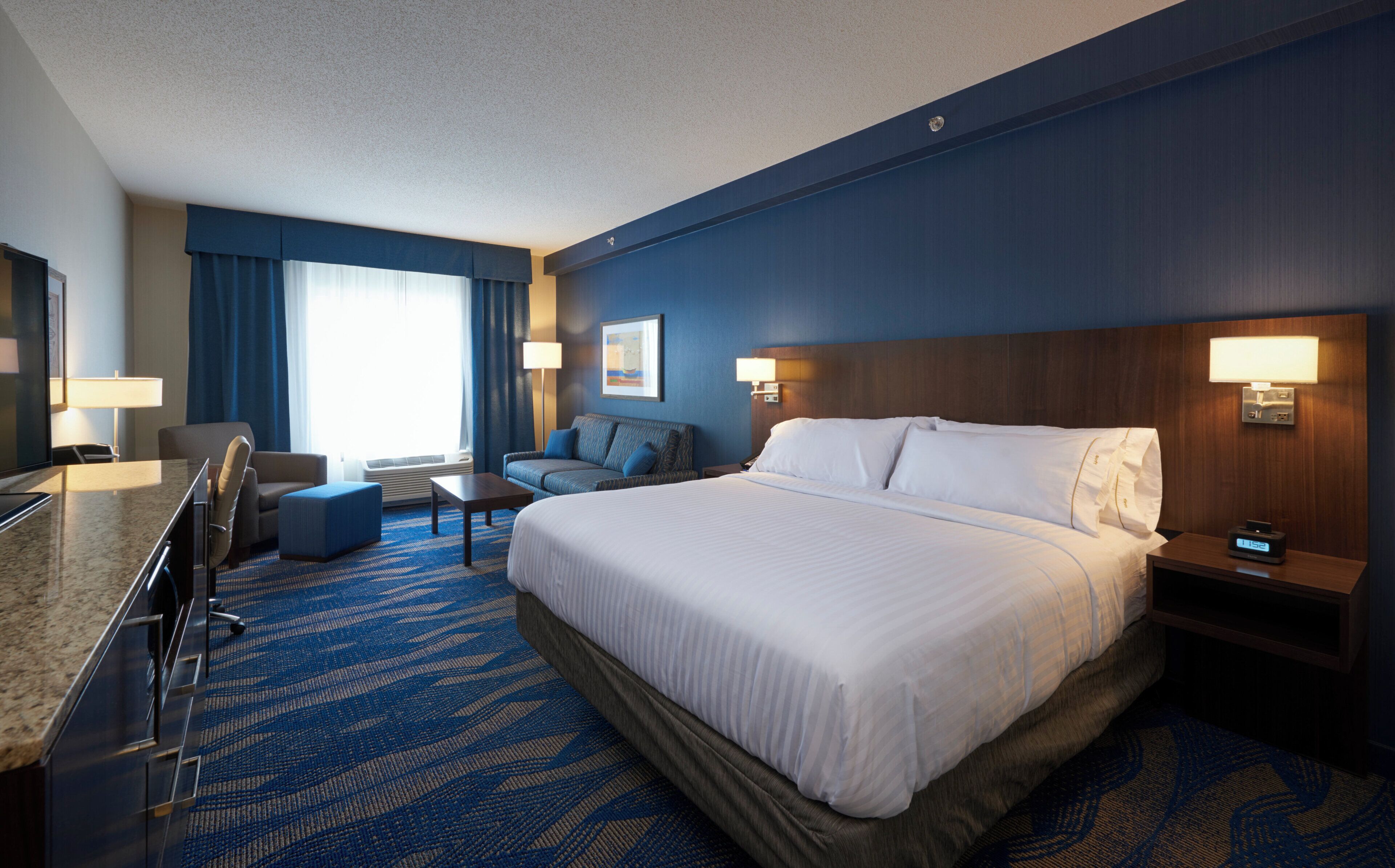 Une chambre d’hôtel avec un grand lit, un bureau, une chaise, un canapé et un téléviseur.