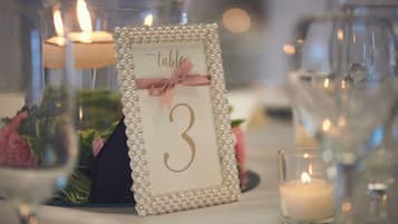 Uma mesa posta com placa numerada, velas e flores decorativas.