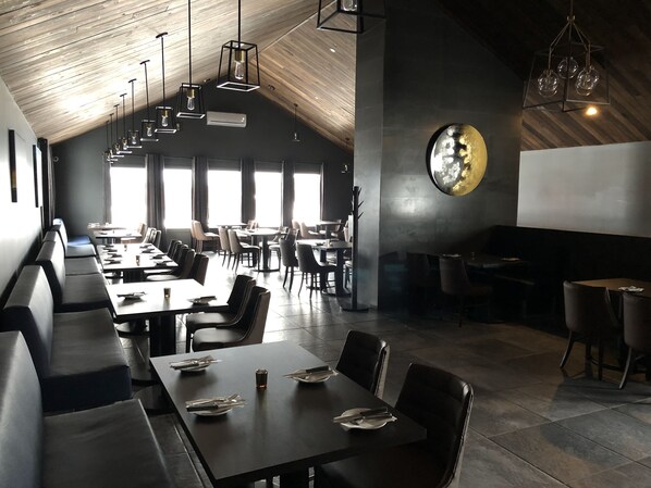 Un restaurant moderne doté de longues tables conviviales, de cabines individuelles et d’un haut plafond avec des poutres apparentes.