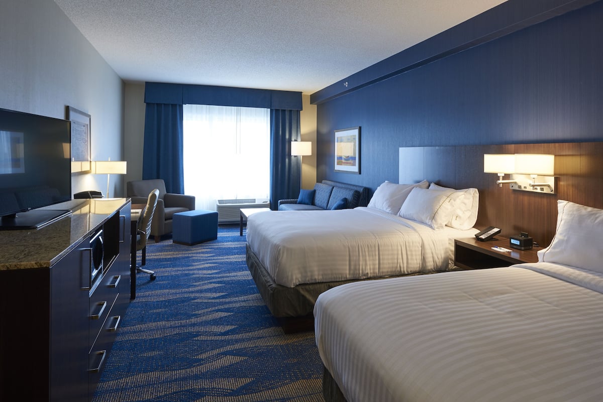 A hotel room with two beds, a desk, a chair, a TV, and a window with curtains.