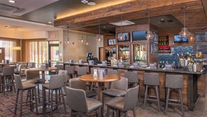 A bar area with multiple seating options, a bar counter with a variety of bottles, and a television screen mounted above the bar.