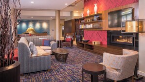 A modern lobby with a sofa, armchairs, a coffee table, a fireplace, and a TV mounted on the wall.