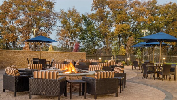 An outdoor patio area with wicker furniture, a fire pit, and blue umbrellas.