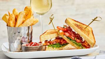 A plate with a grilled sandwich, a glass of white wine, and a container of fries.
