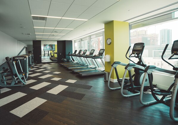 Un gimnasio con cintas de correr, elípticas y un amplio ventanal con vistas a la ciudad.