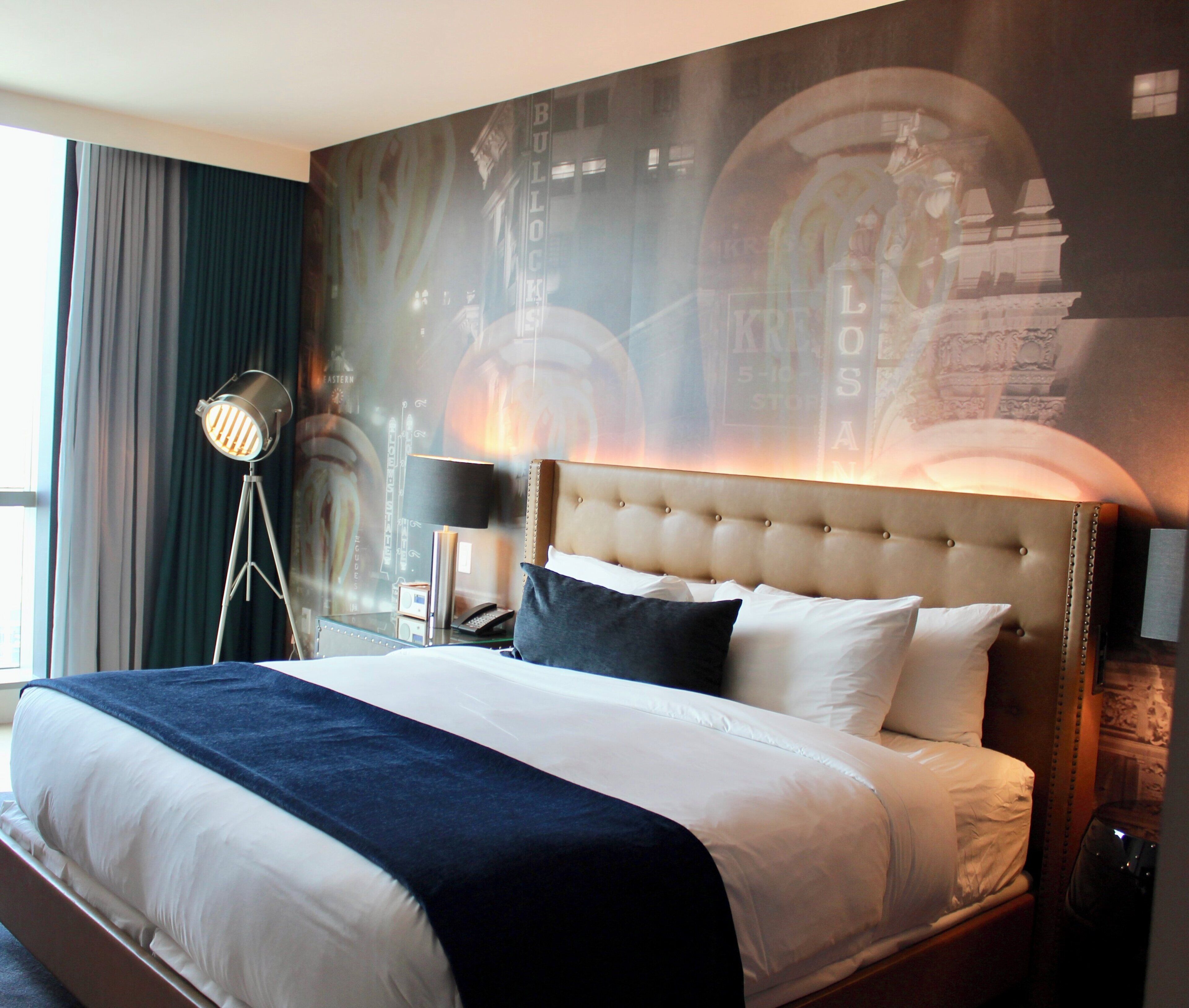 Une chambre d’hôtel avec un grand lit, une tête de lit, une table de chevet, une lampe et un mur orné d’une fresque.