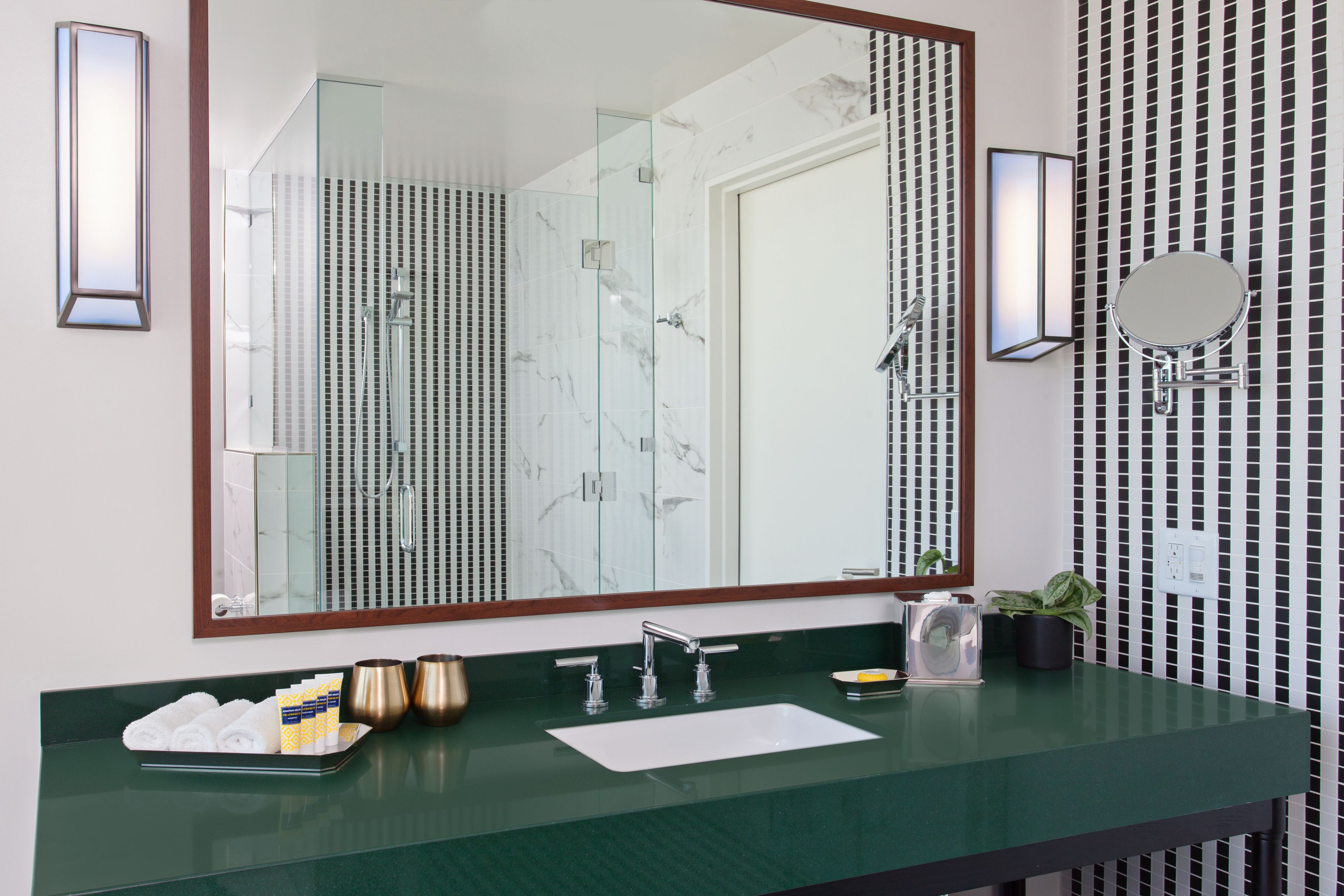 Une salle de bain moderne avec un grand miroir, un plan de toilette vert, un lavabo et un espace douche.