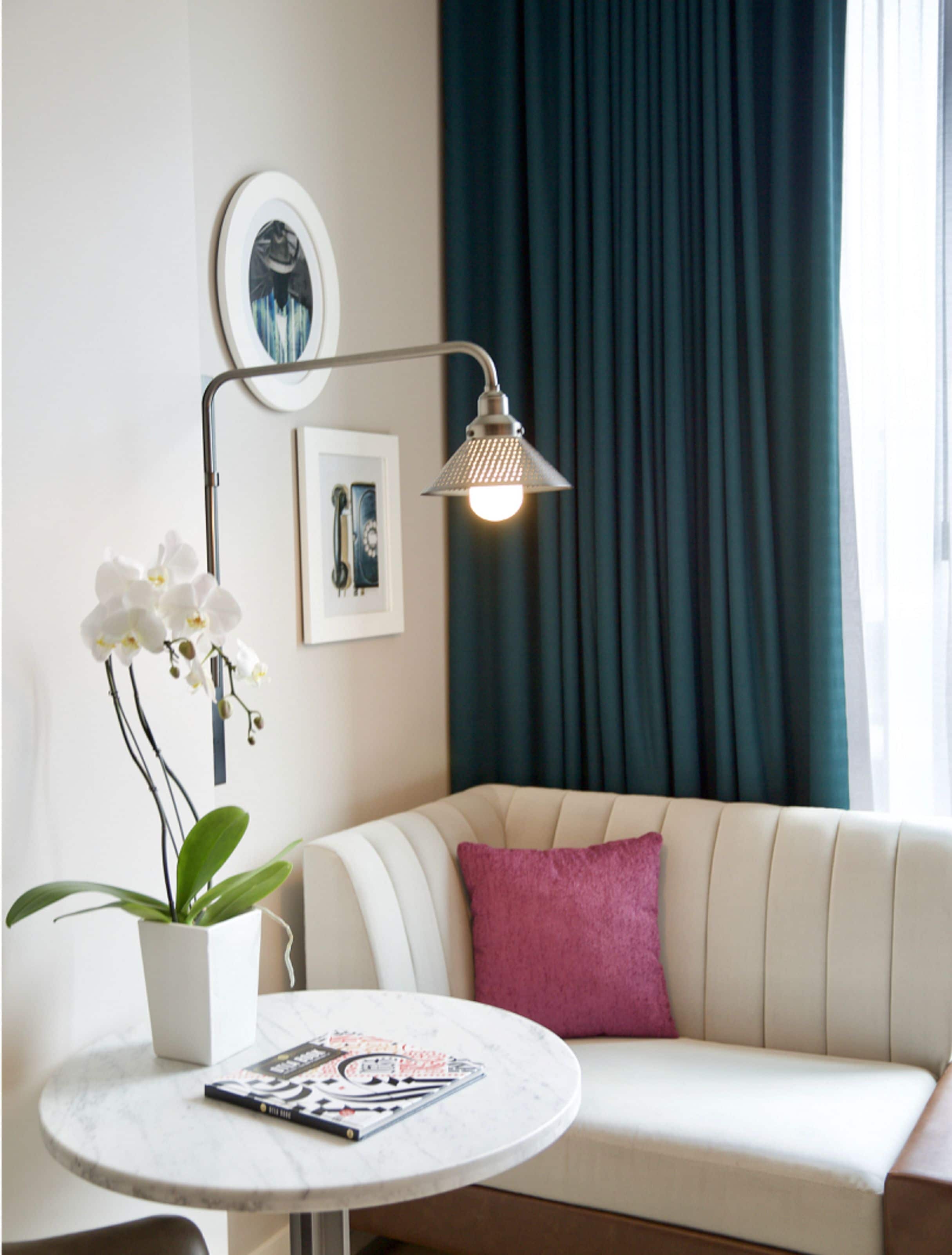 En moderne stue med en hvid sofa, et rundt bord med et magasin, en potte orkidé og en gulvlampe.
