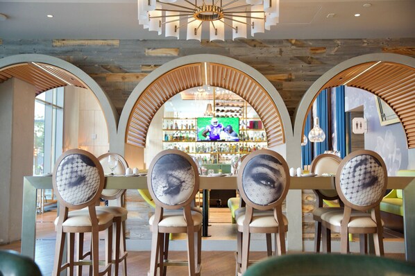 Interior de restaurant amb zona de bar, cadires de fusta amb respatller decorat i un llum modern.