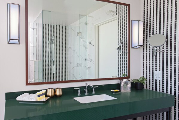 Un baño con un espejo grande, un lavabo, una ducha y un perchero para toallas.