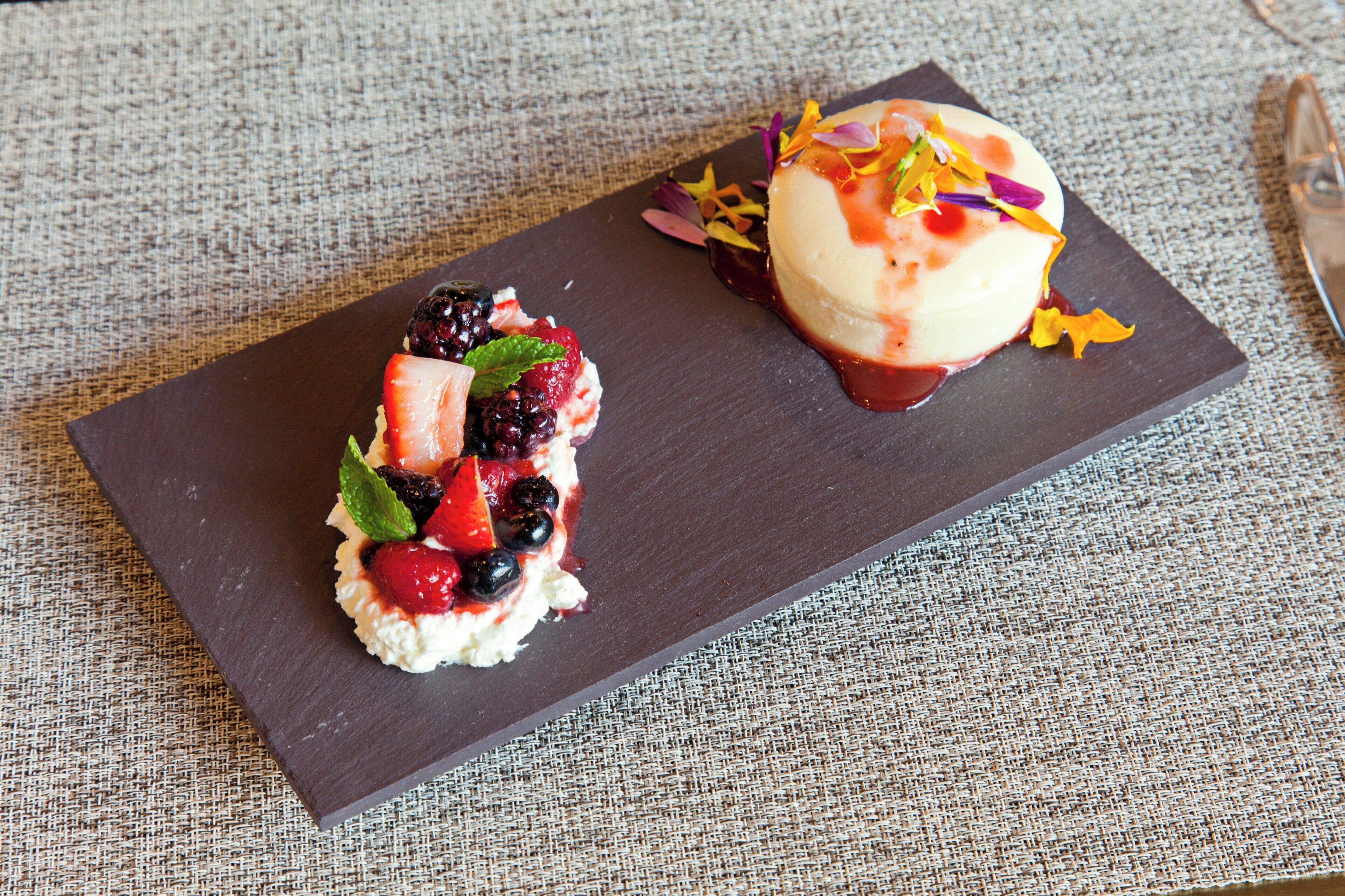 A dessert on a dark slate plate with berries and mint on a textured fabric surface.