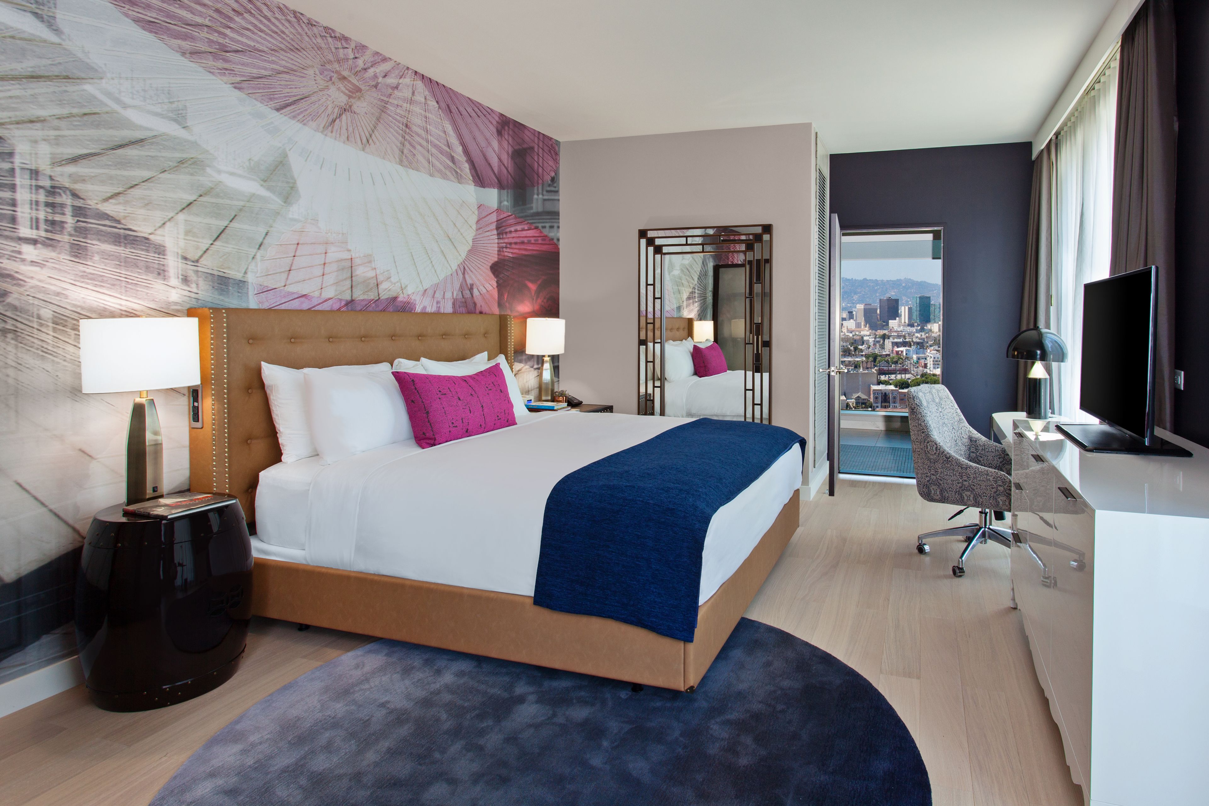 A modern hotel room with a large bed, a desk, and a city view.