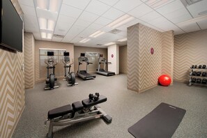 Une salle de sport équipée de tapis de course, d’un banc de musculation, d’haltères et d’un ballon d’exercice rouge.