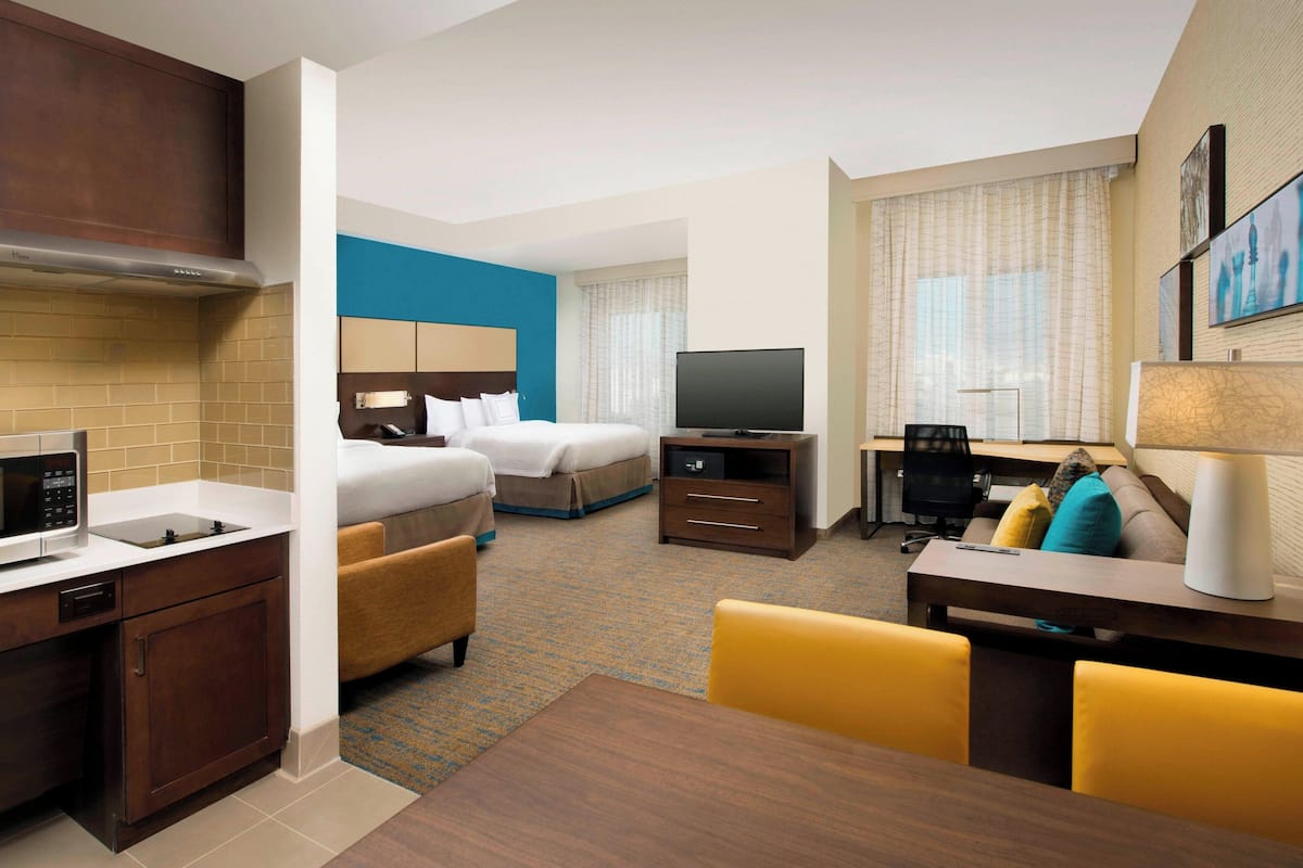 Ein Hotelzimmer mit Küchenzeile, einem Bett, einem Fernseher, einem Schreibtisch und einem Essbereich.