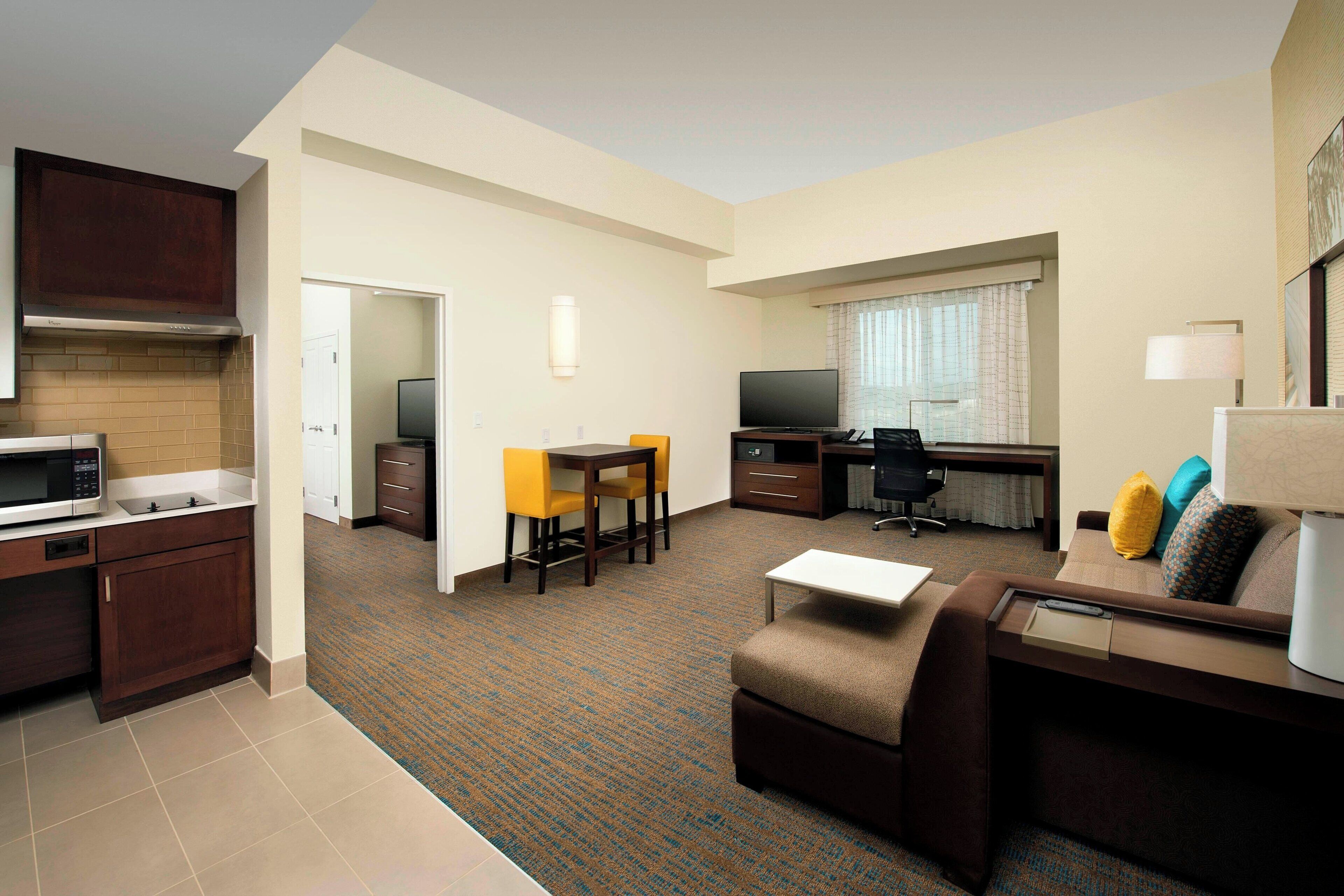 Una habitación de hotel compacta con kitchenette, sofá, escritorio y televisión.