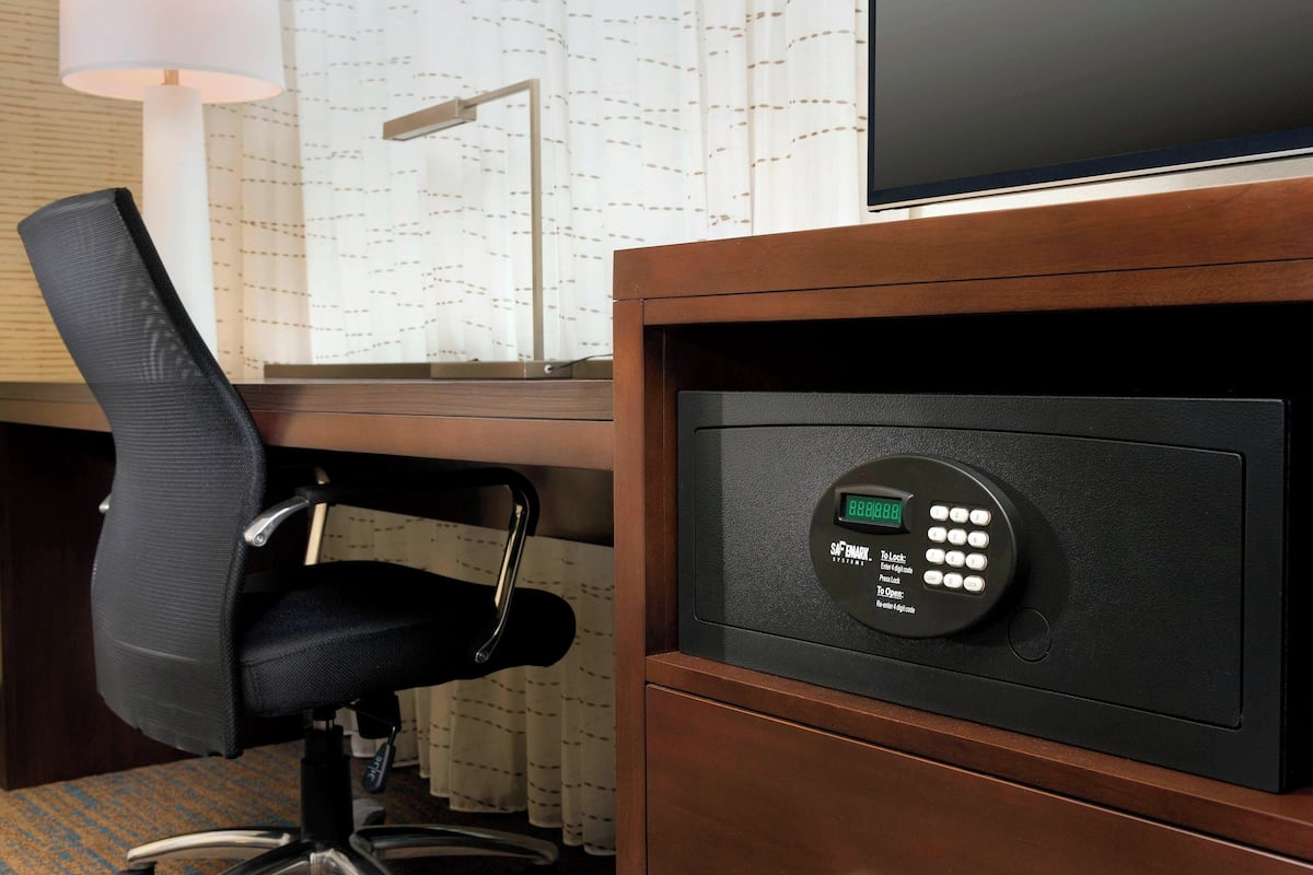 Ein Hotelzimmer mit Schreibtisch, Stuhl, Safe und Fernseher.