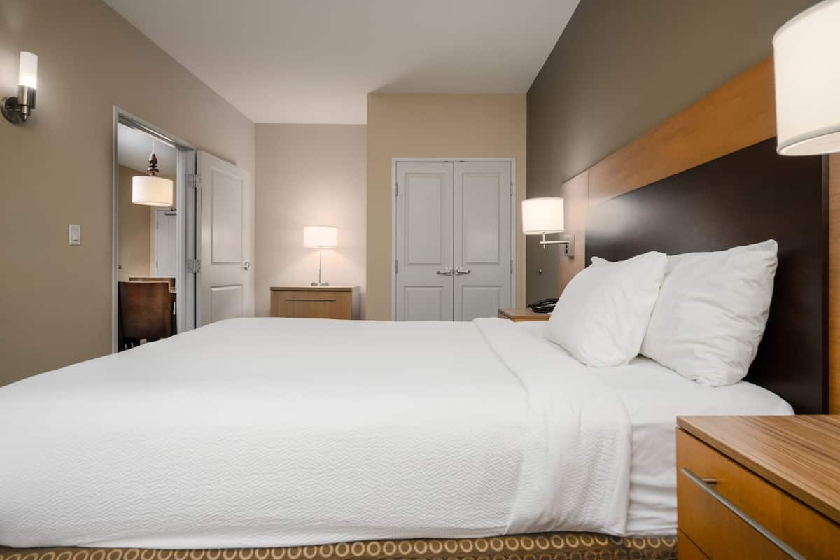 Habitación de hotel con una cama grande, lámparas de noche, un cabecero de madera y una mesita de noche con lámpara.