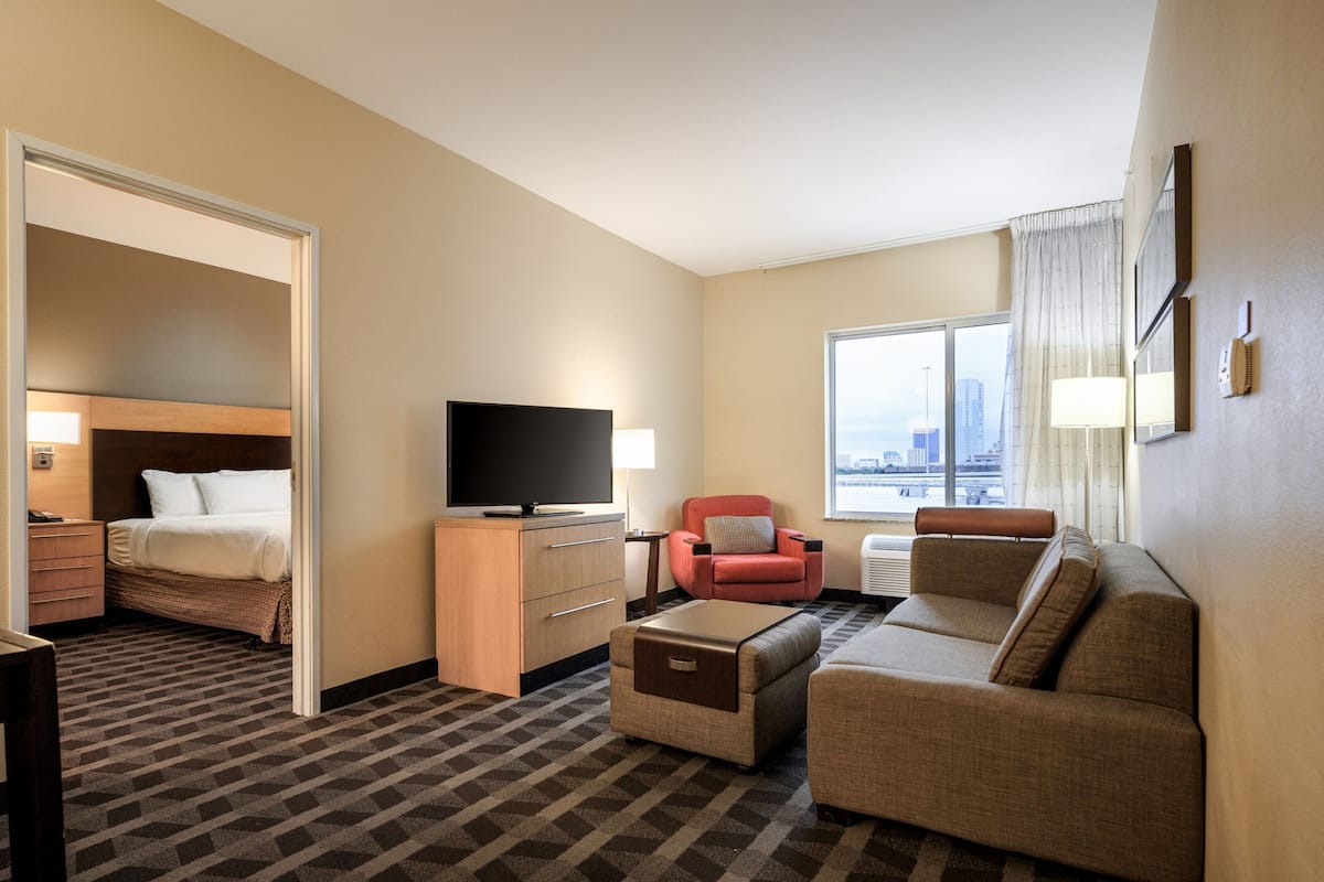 Habitación de hotel con cama, televisión, sofá, sillón y vista a la ciudad.