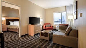 Ein Hotelzimmer mit Bett, Fernseher, Sofa, Sessel und Blick auf die Stadt.