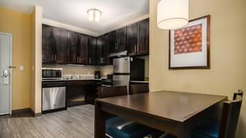A modern kitchen with dark wooden cabinets, stainless steel appliances, and a dining table with blue chairs.