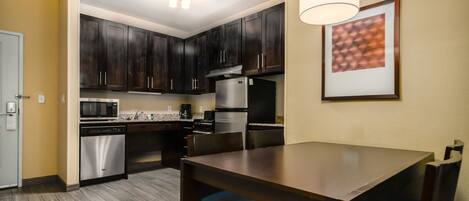 A modern kitchen with dark wooden cabinets, stainless steel appliances, and a dining table with blue chairs.