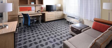 Habitación de hotel con escritorio, silla, televisión y sofá.