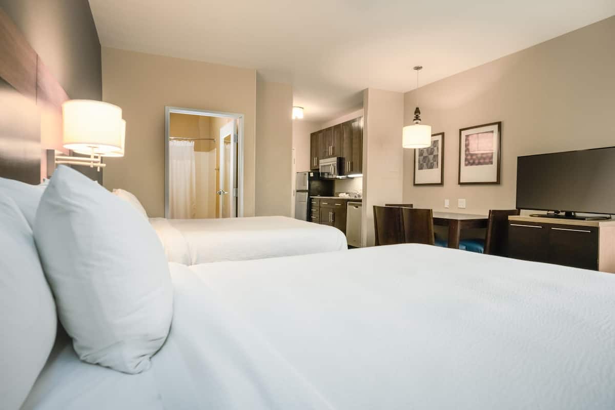 Habitación de hotel con dos camas, kitchenette, televisor y escritorio.
