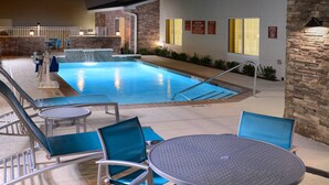 Ein überdachter Swimmingpool mit Steinwand und einer Sitzgelegenheit am Beckenrand mit Stühlen und einem Tisch.