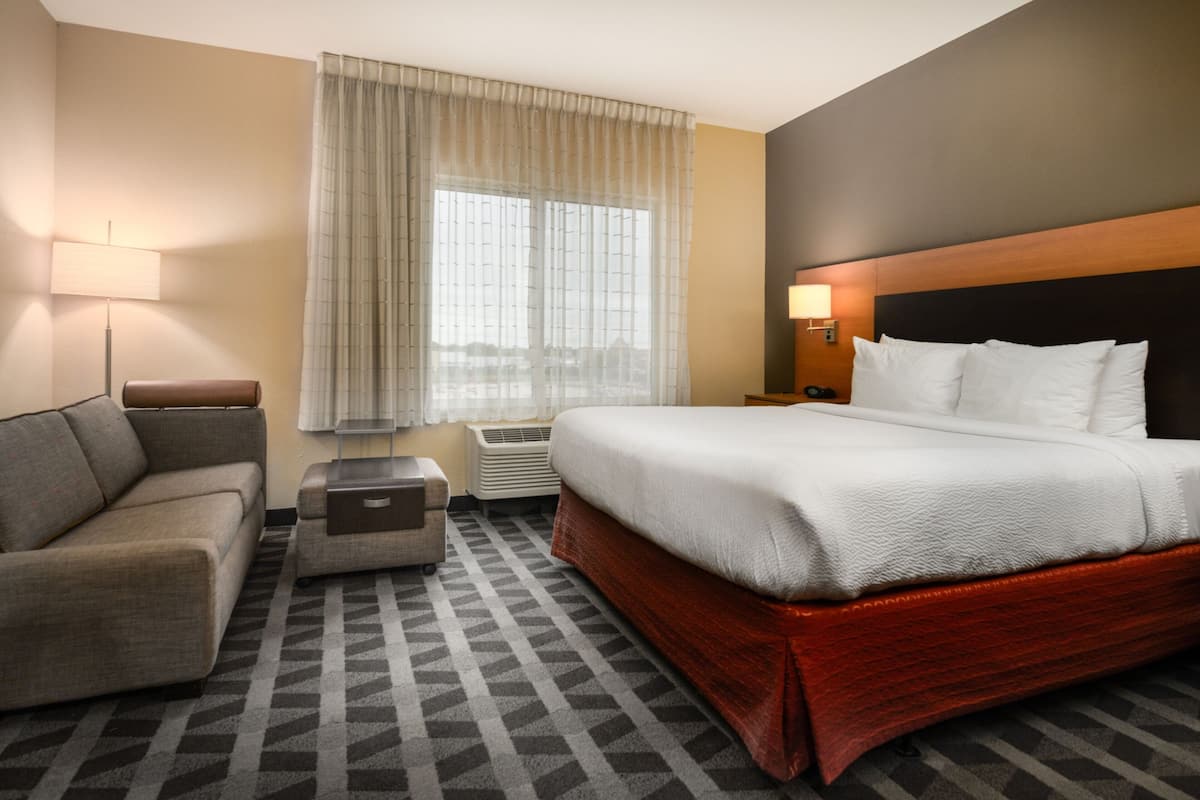Habitación de hotel con cama, sofá, una mesita, lámpara y ventana con cortinas.