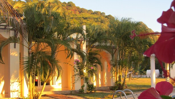 A pool area with a stone pathway, palm trees, and a building with arches. - Marisa Residences (La Gaulette)