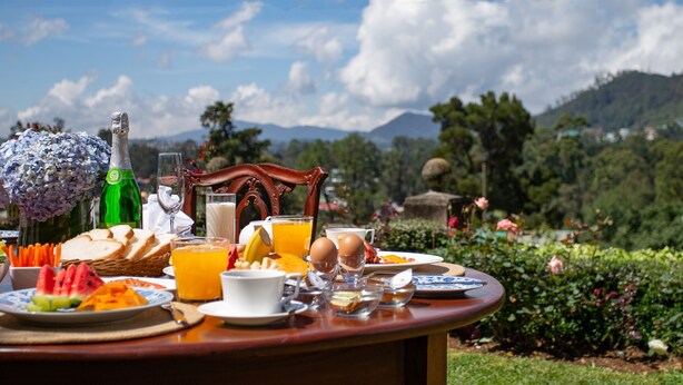 Une table de petit-déjeuner installée à l’extérieur, avec divers aliments, une bouteille et un verre de jus d’orange.
