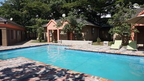 Una piscina con bordes de azulejos, rodeada por una zona pavimentada y un edificio con tejado inclinado.