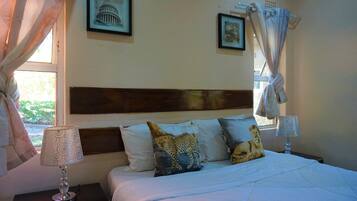 A bedroom with a bed, pillows, a nightstand, a lamp, and curtains.