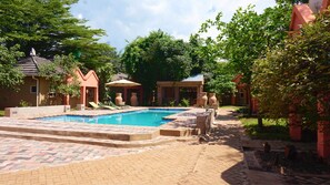 A swimming pool with a tiled deck, surrounded by potted plants and outdoor seating. - Tasha Lodge and Tours (Livingstone)