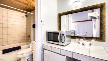 A bathroom with a bathtub, toilet, and a microwave on the counter.