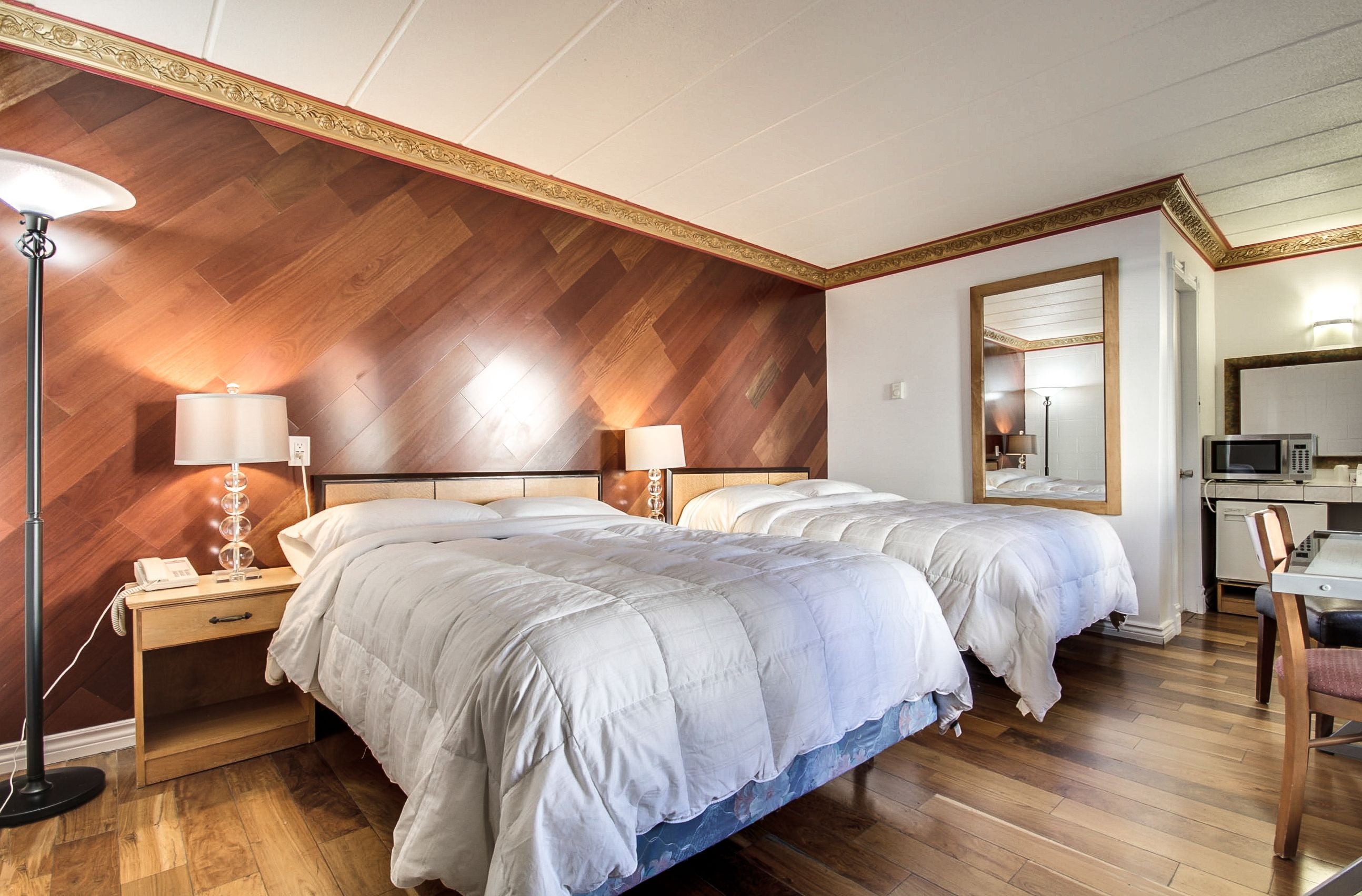 Habitación de hotel con dos camas, un escritorio, una silla, un microondas y una mesita de noche con lámpara.