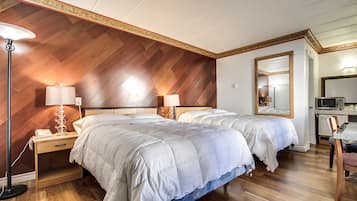 Habitación de hotel con dos camas, un escritorio, una silla, un microondas y una mesita de noche con lámpara.